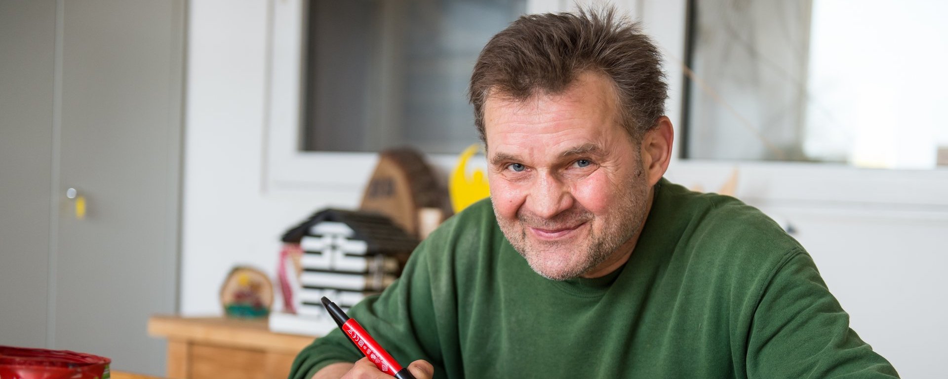 Mann mit Lötkolben sitzt am Tisch und "graviert" Baustamm-Abschnitte