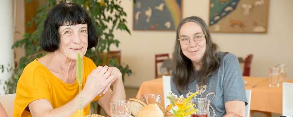 zwei glücklich wirkende Frauen sitzen am Frühstückstisch bei Brot, Brötchen und schön garniertem Wurstaufschnitt