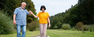 Eine Frau geht über den Barfußpfad - ein Mann hält ihr helfend die Hand