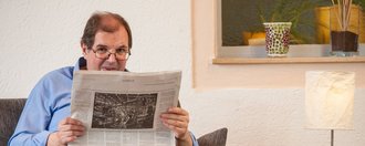 Ein Mann mit Brille sitzt in einem Ledersessel und liest Zeitung